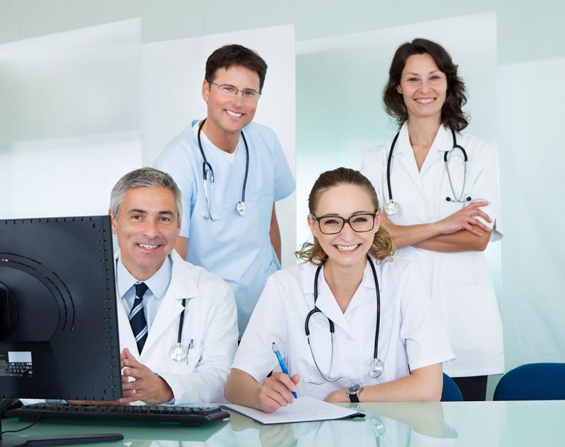 Health care workers wearing lab coats, scrubs and stethoscopes in a small office. 