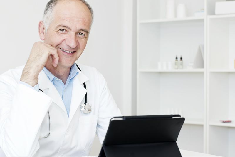 Doctor wearing coat and stethoscope working on a tablet. 